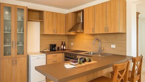 A modern kitchen with wooden cabinets, a built-in dishwasher, and a central island with bar stools. - Villa Flavia - Luxury Retreat (Polignano a Mare)