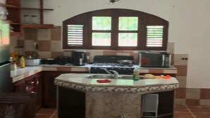 Una cocina con una isla central, estufa, microondas y pileta. Hay alacenas y una lámpara colgante.