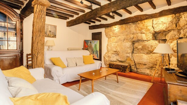 Un salón acogedor con un sofá blanco, cojines amarillos, una mesa de centro de madera y una pared de piedra.