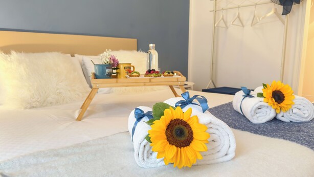 Un lit bien fait, avec du linge de lit blanc, un plateau contenant des articles pour le petit-déjeuner et des serviettes ornées de motifs de tournesols.