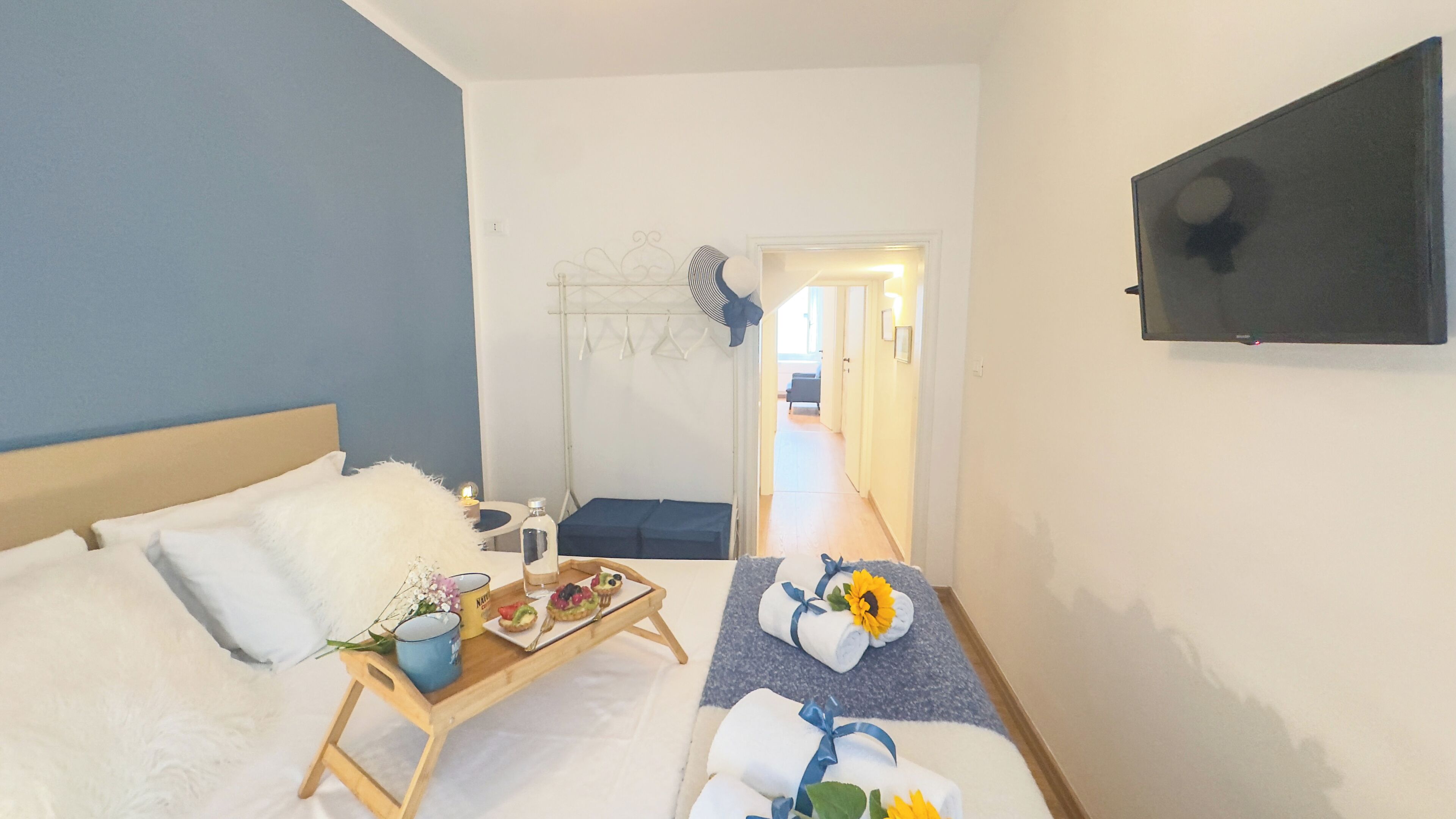 A hotel room with a bed, a small table with a tray of food, a wall-mounted TV, and a door leading to another room.