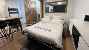 Quarto de hotel com cama, escrivaninha, cadeira, espelho e mesa pequena.