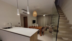 A modern kitchen with a central island, a dining area with a wooden table and chairs, a sofa, and a staircase leading to another level. - Lovely 3 beds 3 baths Penthouse with Rooftop Pool (Punta Cana)