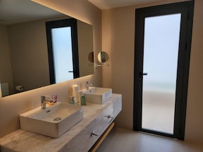 A modern bathroom with two sinks, a large mirror, and a view through a glass door.