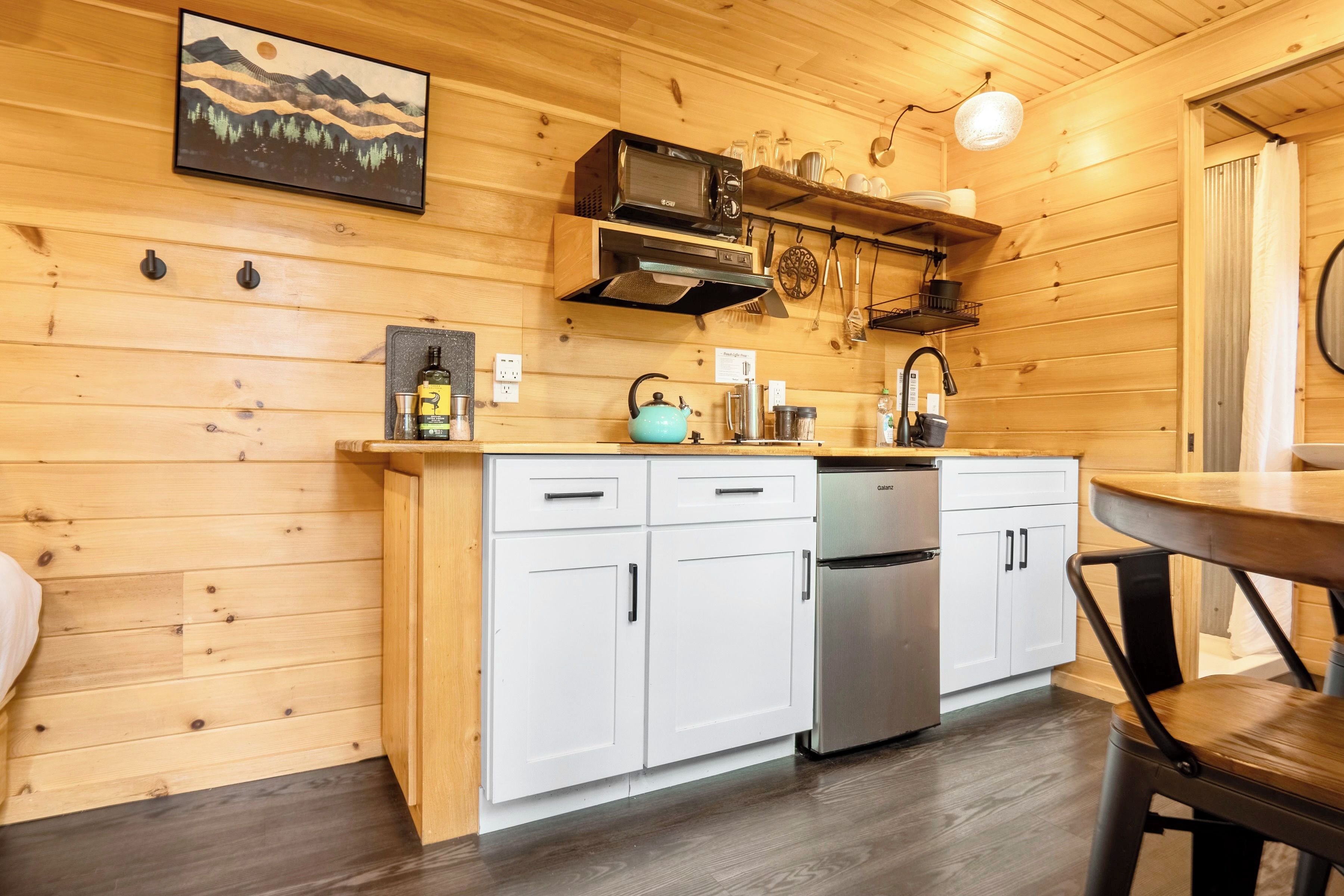 A wooden interior with a kitchen area featuring a refrigerator, a microwave, and a kettle.