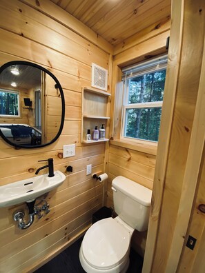Baño de cabaña de madera con lavabo, inodoro, espejo y ventana.