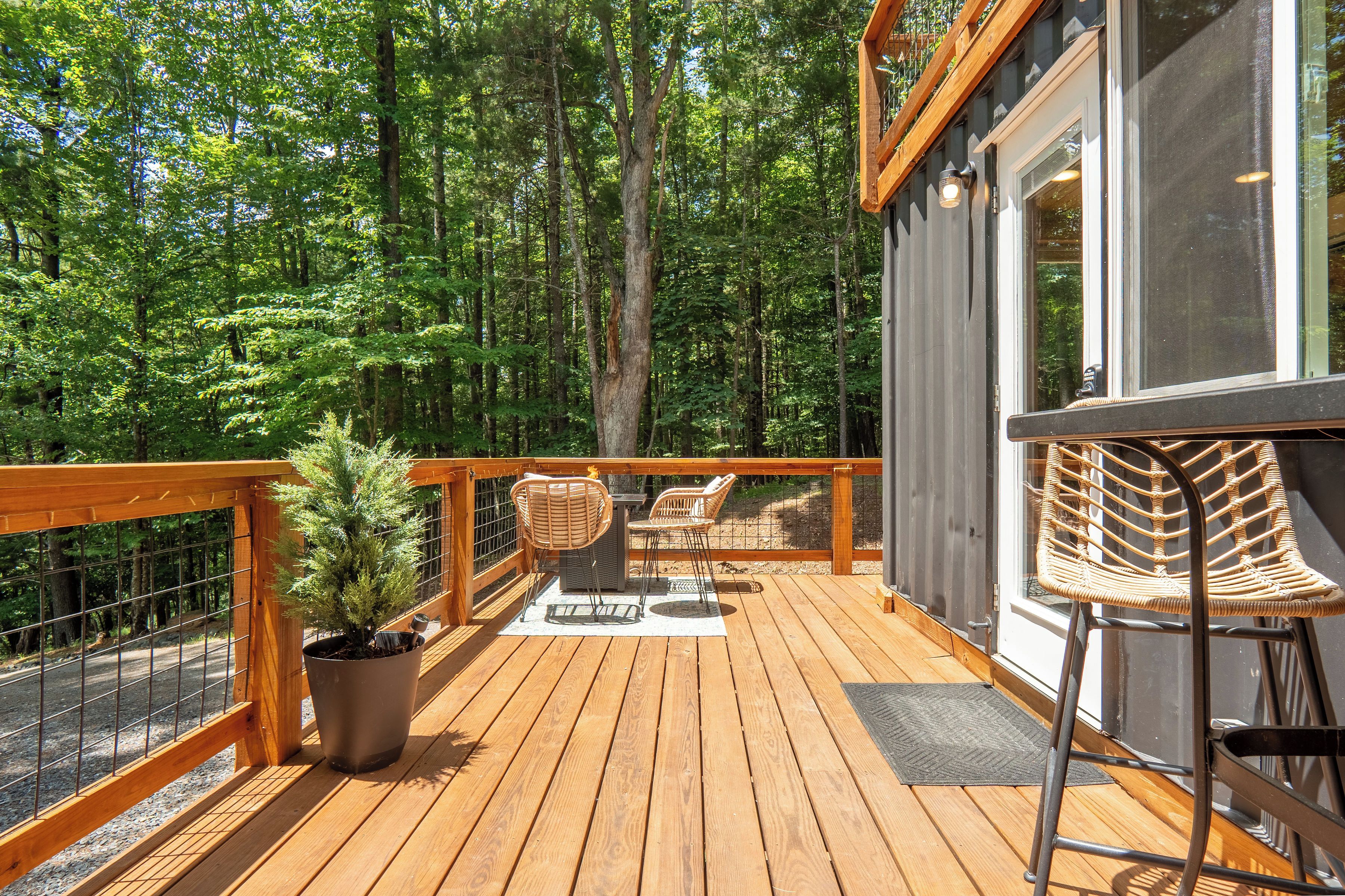 A wooden deck with a railing, a potted plant, two wicker chairs, and a table.