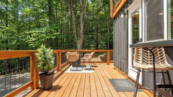 A wooden deck with a railing, a potted plant, two wicker chairs, and a table.