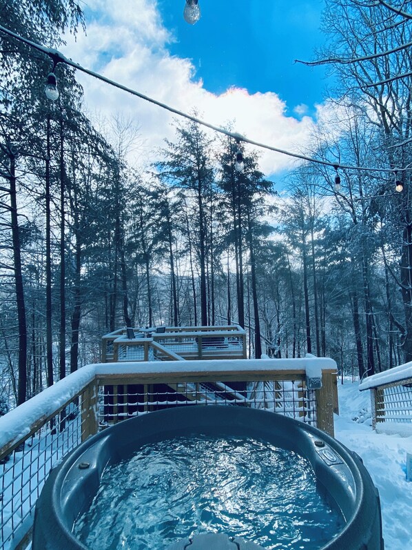 Un bain à remous entouré d’arbres couverts de neige et doté d’une terrasse en bois.