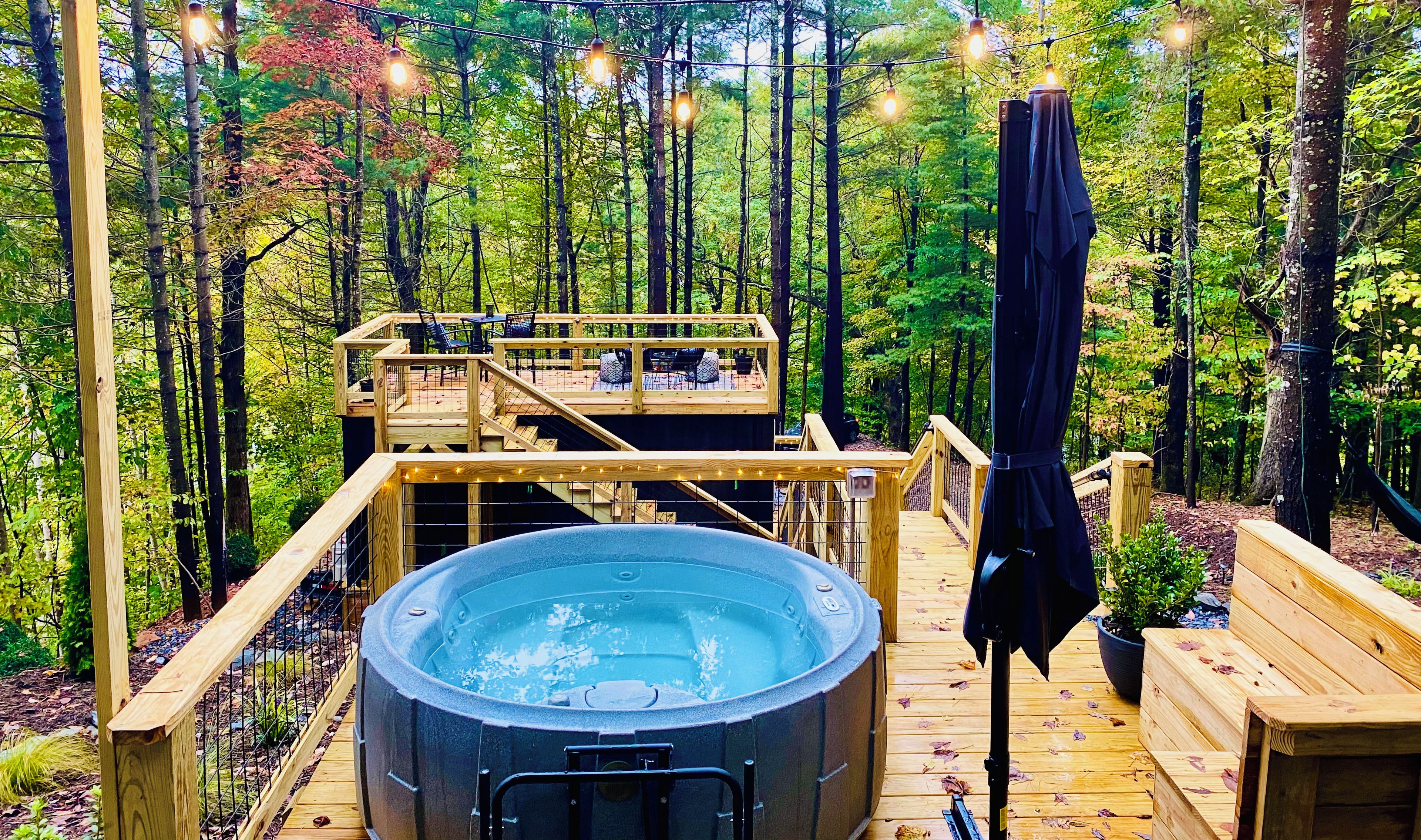 A hot tub on a wooden deck surrounded by a forest, with a wooden deck chair and a bench.