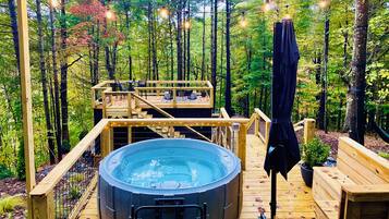 A hot tub on a wooden deck surrounded by a forest, with a wooden deck chair and a bench.