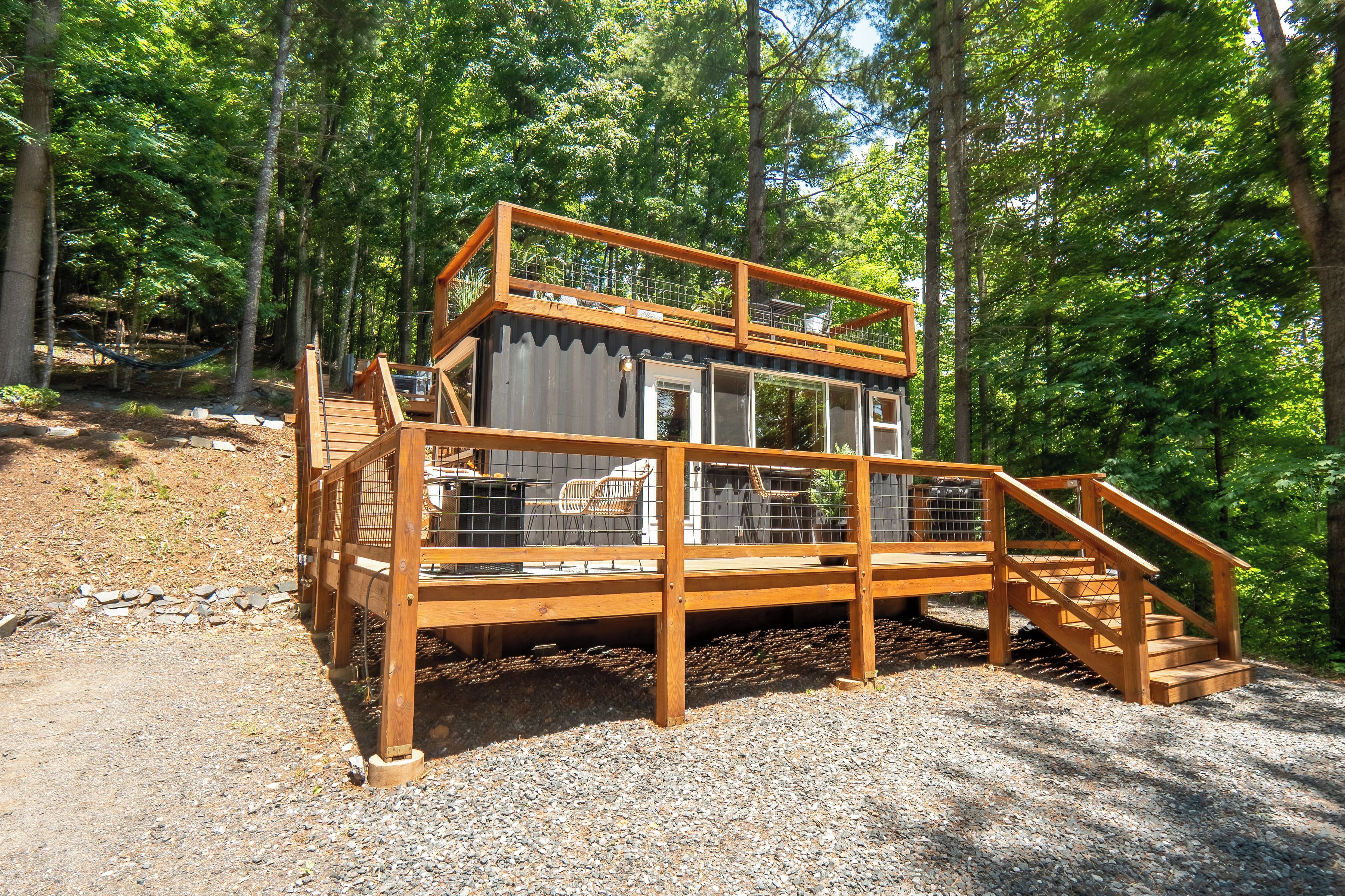 A wooden cabin with a balcony, a staircase, and a gravel ground.