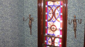 A room with a stained glass window, patterned wallpaper, and a chandelier.