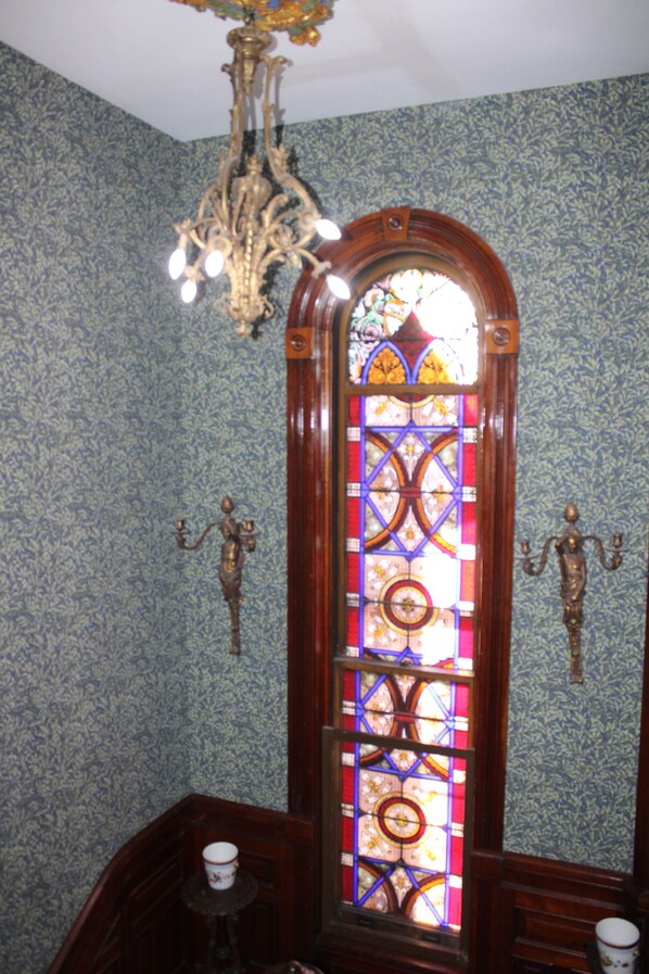 A room with a stained glass window, patterned wallpaper, and a chandelier.