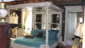 A four-poster canopy bed with a teal bedspread, a wooden headboard, and a nightstand with a lamp.