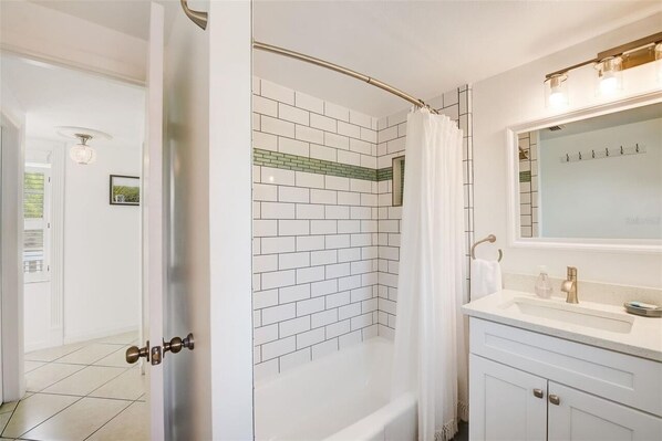 A bathroom with a white tiled shower, a white sink with a gold faucet, and a mirror above the sink.