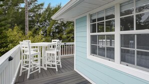 Une terrasse couverte avec une table et des chaises blanches, entourée d’un bâtiment bleu clair doté de grandes fenêtres.