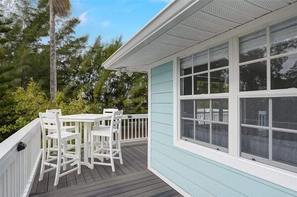 A covered deck with a white table and chairs, surrounded by a light blue building with large windows.