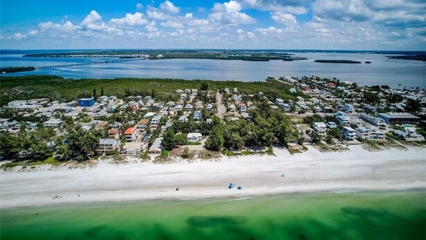 Vue aérienne d’une zone résidentielle côtière, avec des maisons, une plage et un pont en arrière-plan.