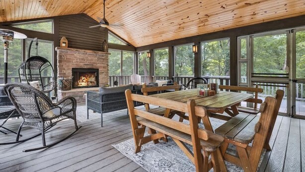 A wooden deck with a stone fireplace, outdoor seating, and large windows.
