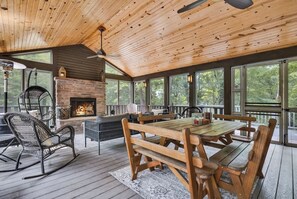 Une terrasse en bois avec une cheminée en pierre, des sièges d’extérieur et de grandes fenêtres.