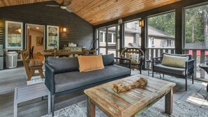 A cozy interior with a wooden ceiling, large windows, a sofa, a coffee table, and a dining area.