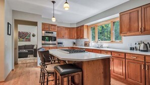 A modern kitchen with wooden cabinets, a central island, bar stools, and a large window.