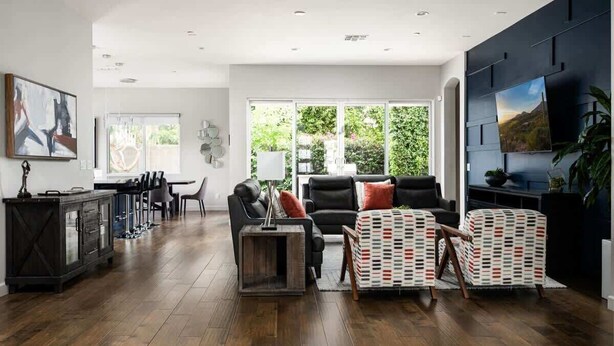 Un salon moderne avec un parquet en bois foncé, un canapé en cuir noir, des fauteuils à motifs et un téléviseur fixé au mur.