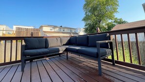 Una terraza de madera con un sofá de color oscuro y una barandilla metálica.