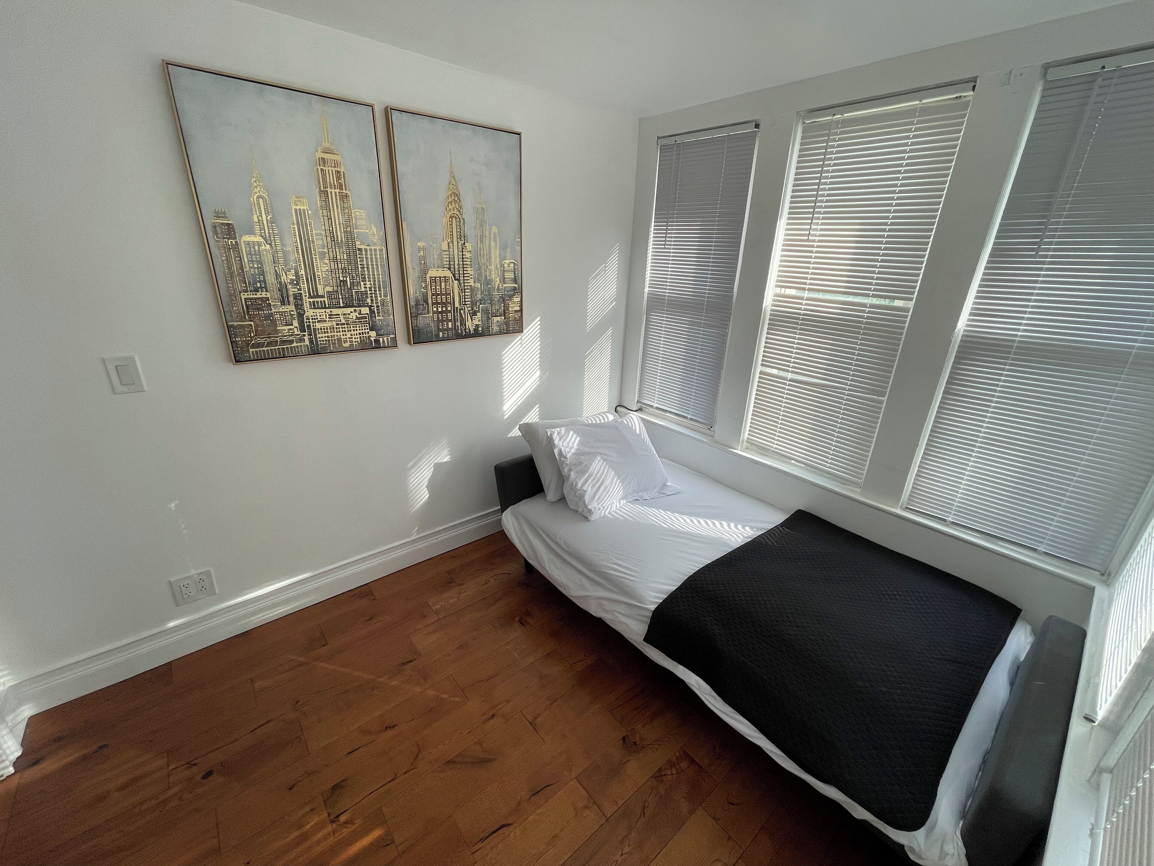 A bedroom with a bed, two wall-mounted paintings, and a window with blinds.