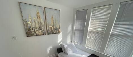 A bedroom with a bed, two wall-mounted paintings, and a window with blinds.