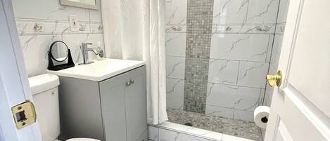 A bathroom with a toilet, sink, mirror, shower with a glass door, and tiled floor.
