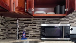 Una cocina con armarios de madera, encimera de granito, microondas y un lavabo.