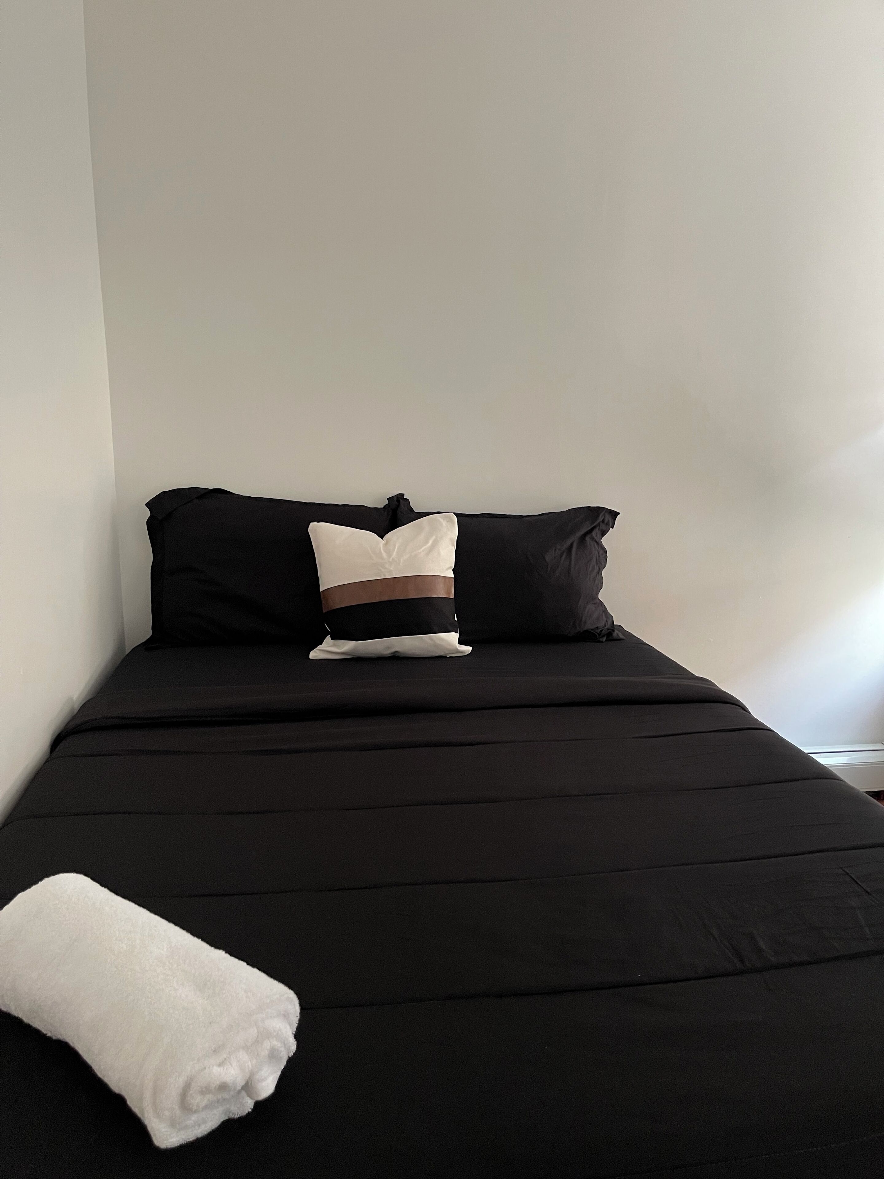 Ein Einzelbett mit schwarzer Bettwäsche, zwei Kissen und ein weißes Handtuch.