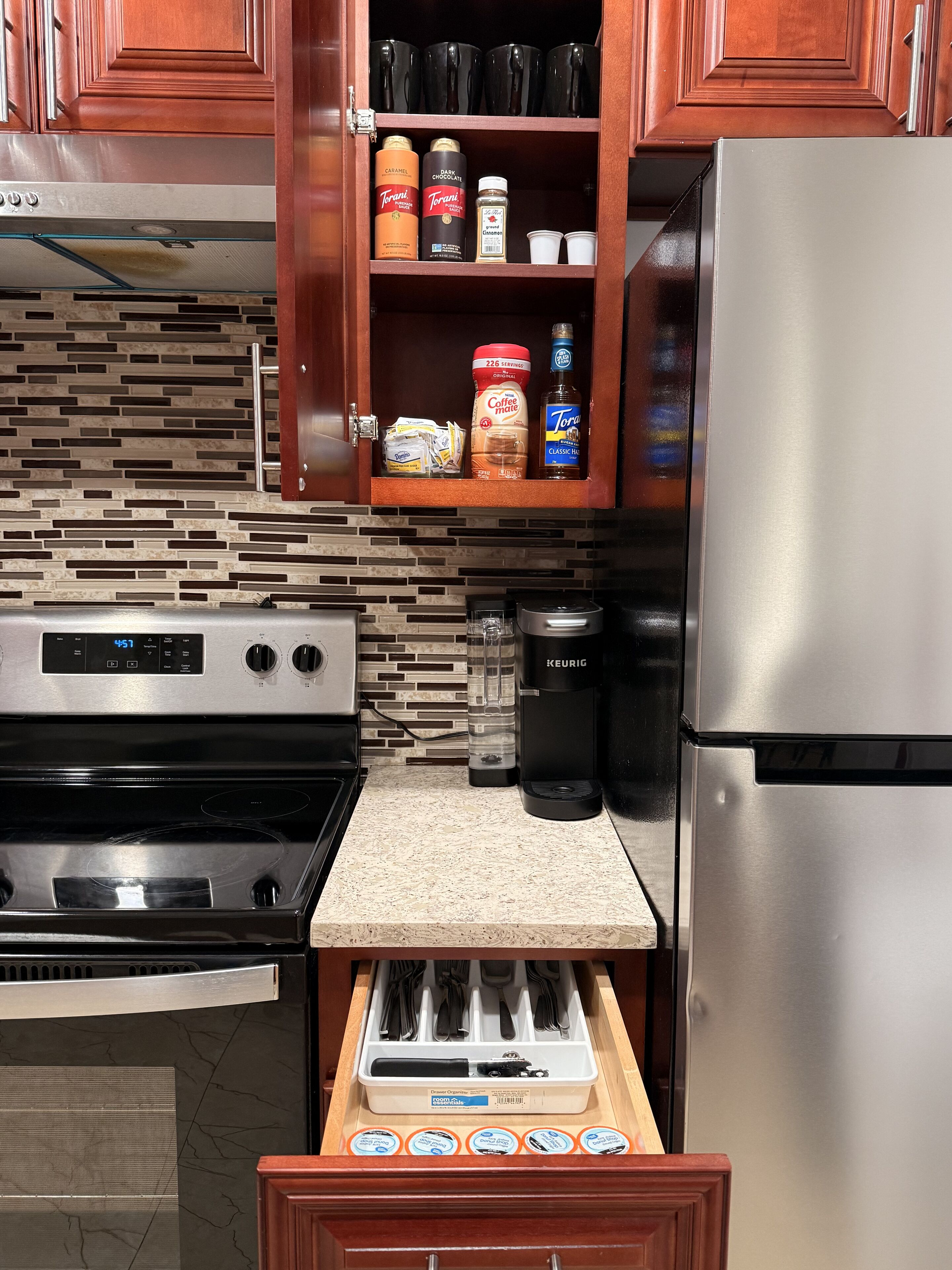 A kitchen with a stainless steel refrigerator, a coffee maker, a toaster, and a drawer organizer with utensils.
