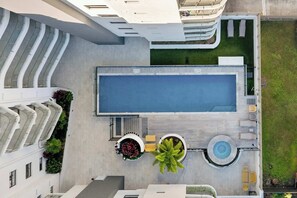 Vista aérea de um hotel moderno com piscina no terraço, área de estar externa e jardim ajardinado.