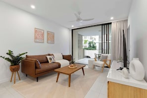 A modern living room with a brown sofa, a wooden coffee table, a white armchair, and a glass door leading to a balcony.