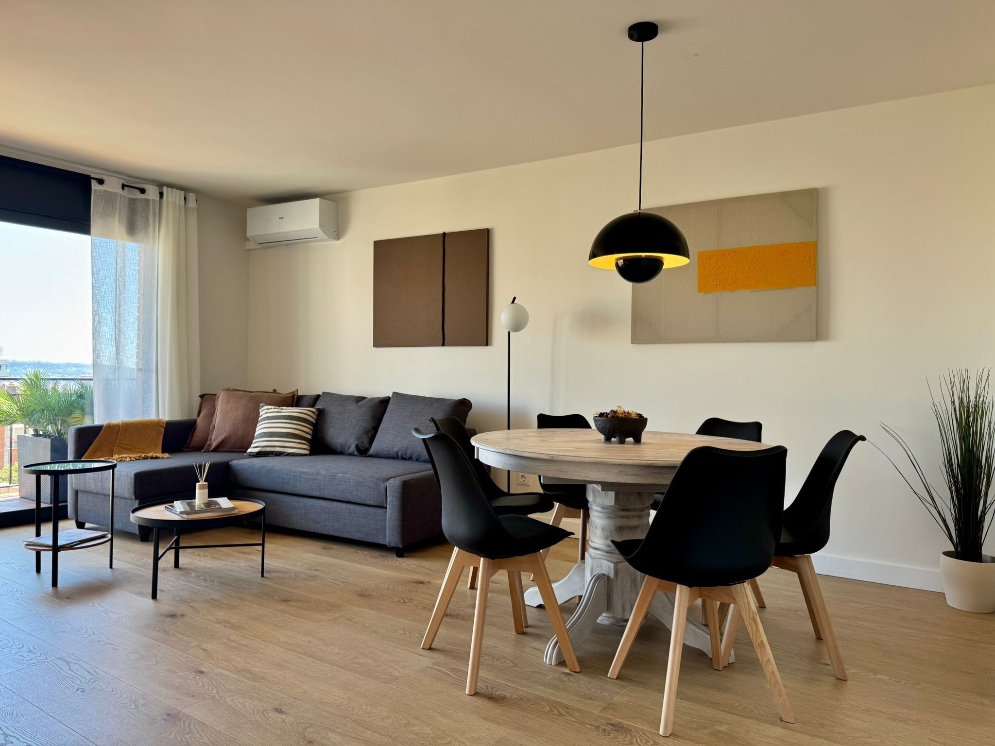 A modern living room with a grey sofa, black chairs, a round wooden table, and a pendant light.