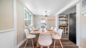 Comedor con mesa de madera, sillas blancas y una lámpara de araña.