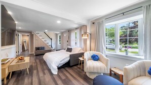 Un dormitorio moderno con cama, sofá, sillón, una mesita y ventana con vistas al exterior.