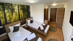 Een hotelkamer met twee bedden, een grote bosmuur, een spiegel en een televisie.
