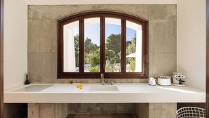 A modern kitchen with a large white countertop, a built-in sink, and a window with a wooden frame. - Luxury villa with private pool | Villa Arabesca (Selva di Fasano)