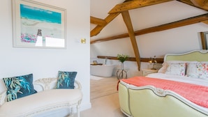 A bedroom with a bed, a chair, a painting, and a bathroom with a bathtub. - Bay View - sleeps 6 guests  in 3 bedrooms (Nefyn)