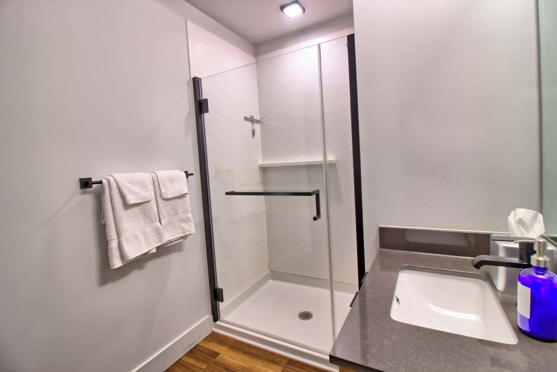 A modern bathroom with a glass shower enclosure, a white sink, and a towel rack.