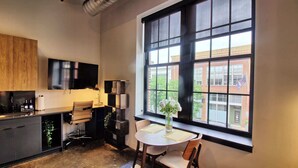 A modern kitchen with a large window, a dining area with a table and chairs, and a flat-screen TV mounted above the counter. - Chic Ultramodern Studio Loft w/ Designer Features (St. Louis)