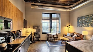 A compact hotel room with a kitchenette, a dining area, a sofa, and a bed. - Chic Ultramodern Studio Loft w/ Designer Features (St. Louis)