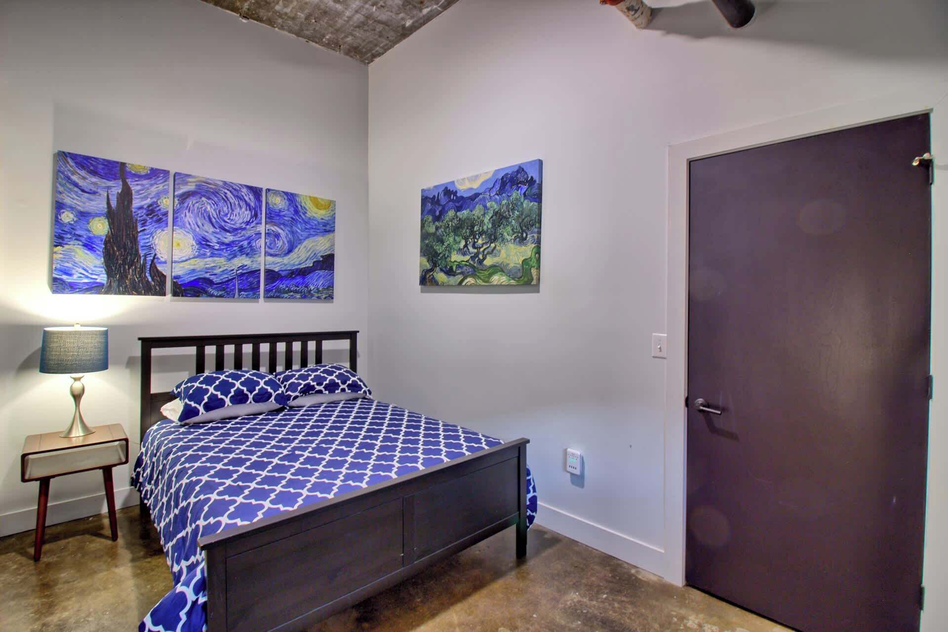 A bedroom with a bed, a nightstand, and two wall-mounted paintings.
