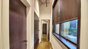 A hallway with dark wooden doors, a window with blinds, and a concrete floor.