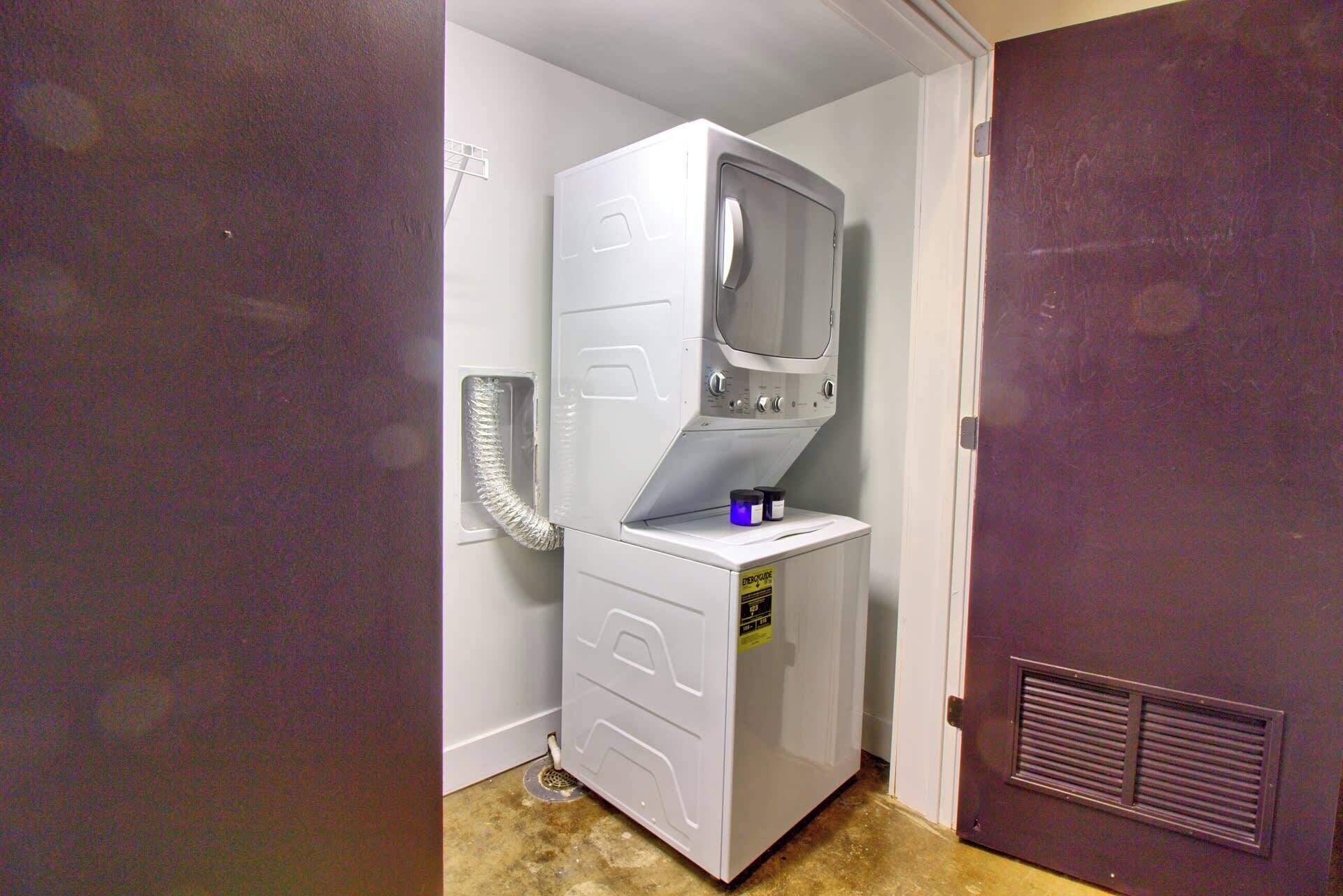 A compact laundry room with a stacked washer and dryer, a vent hose, and a door with a vent grille.