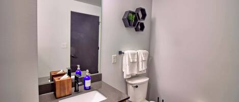 A modern bathroom with a large mirror, a sink with a wooden cabinet, a toilet, and a towel rack.